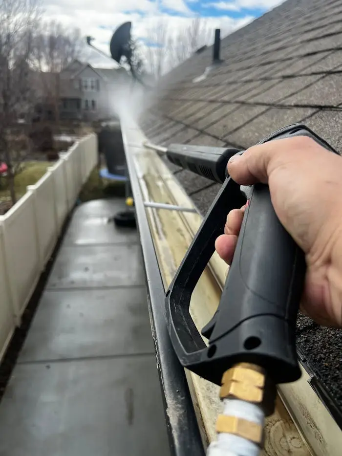 Close-up of gutter cleaning with pressure washer, outdoors, during the day.